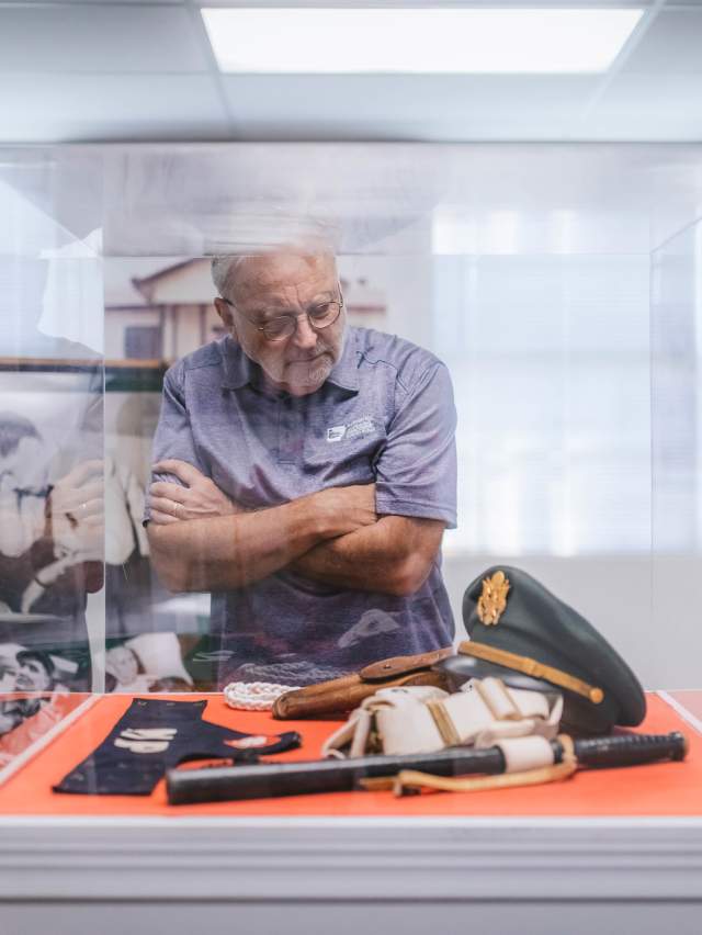 A man peers into a glass box filled with Elvis memorabilia at the Chaffee Barbershop Museum, his arms crossed.