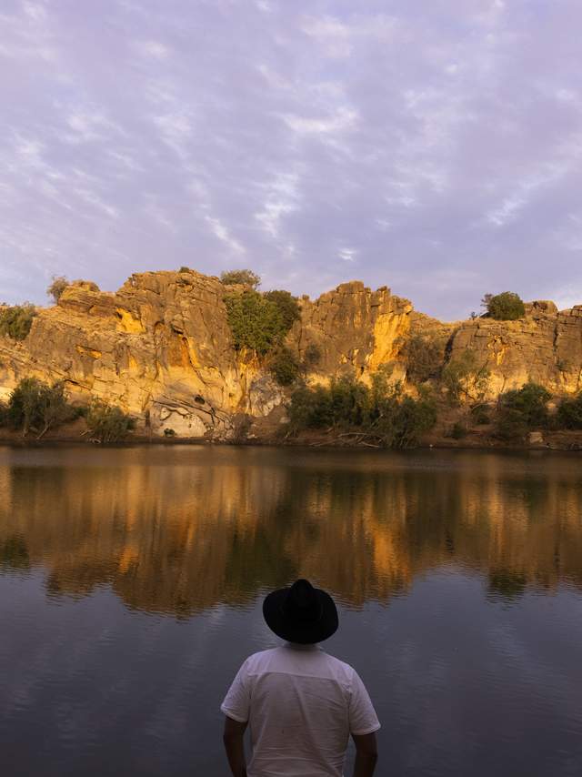 A man stands on the banks of Danggu Geikie Gorge looking across the water.