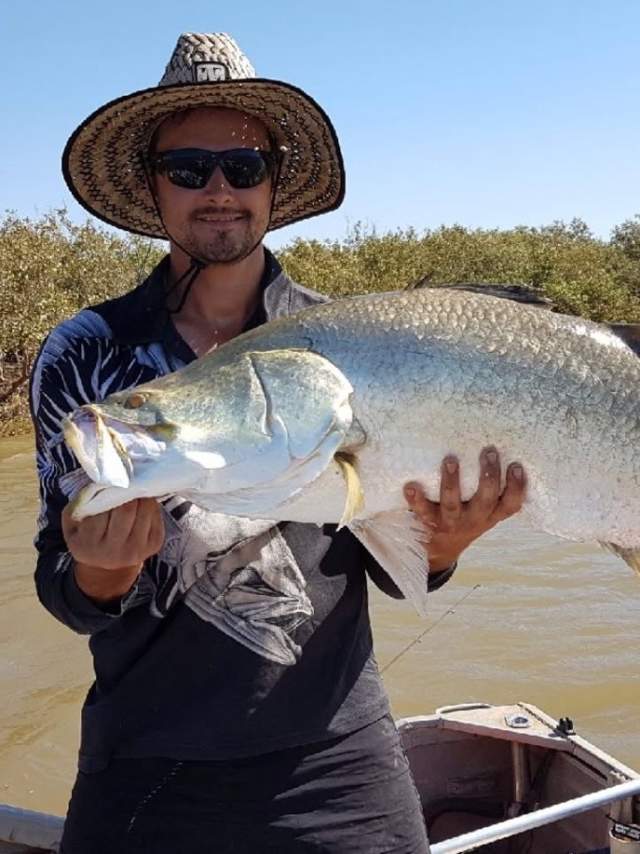 A man in a tinny holding a freshly caught barra, in a creek near Port Hedland