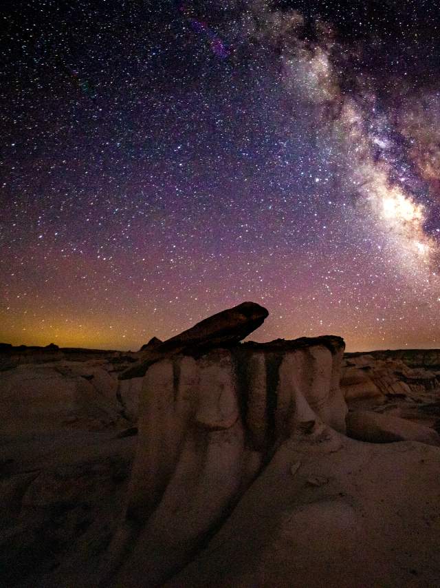shadowed rock formations span far into the distance, beneath a bright constellation of stars spanning the entire sky