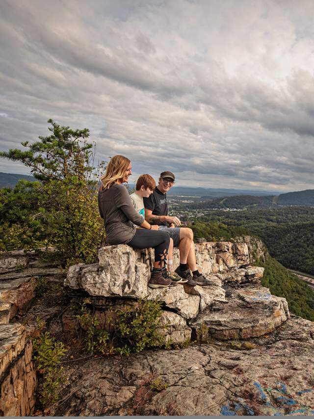 A mom, dad and son sit on a shale cliff overlooking a mountain vista.
