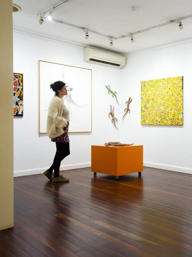 A woman looking at artworks in the Courthouse Gallery, Port Hedland. The walls are hung with colourful paintings, with some small sculptures also mounted on the walls.