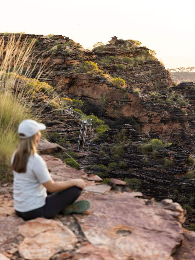 A woman sits on a rock in Mirima National Park, looking out across the striped rock formations