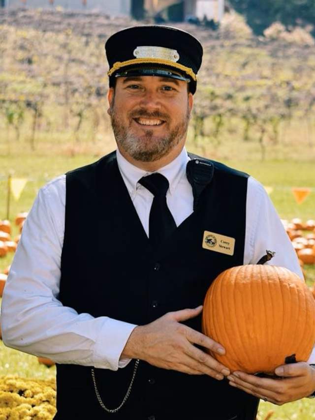 A train conductor smiles with a pumpkin at Heart of Dixie Railroad Museum.