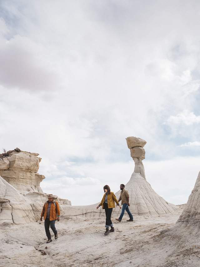 Three people wearing outdoor exploration clothing walk amongst the towering white stone structures