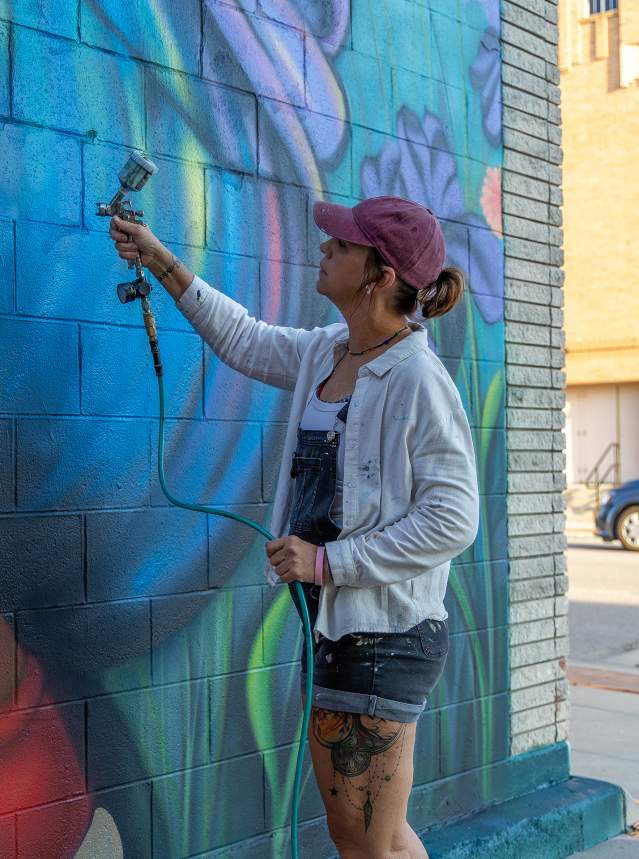 Artist Mindy Allen painting her mural titled Stop and smell the flowers as part of the BOOM! Salina mural festival