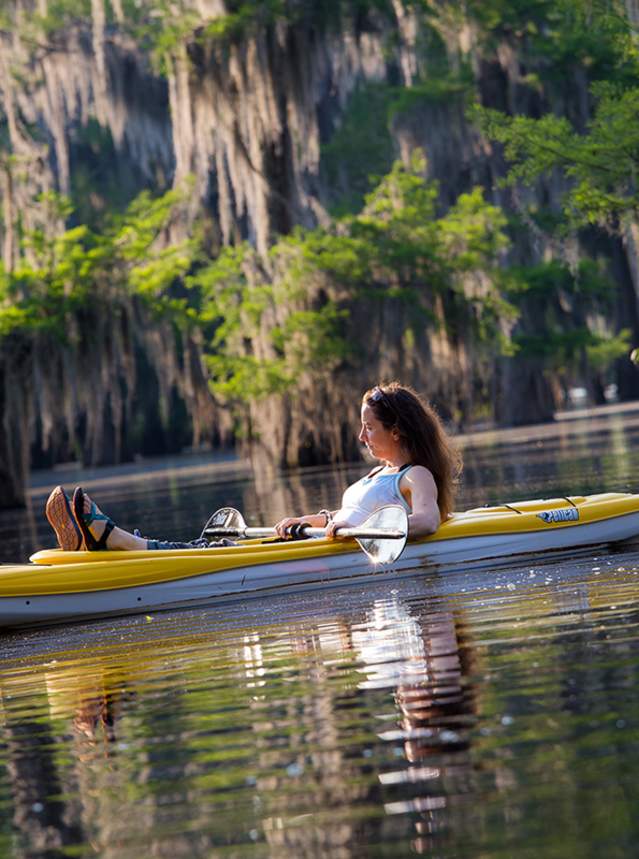 Kayaker on lake under cypress trees with hanging Spanish moss
