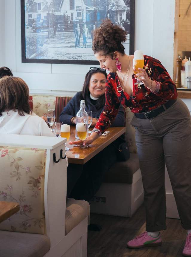 Server bringing pints to visitors sitting in a booth. Patrons are smiling.