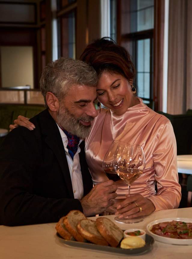 Couple holding each other. Wine in hand and small bites around them.