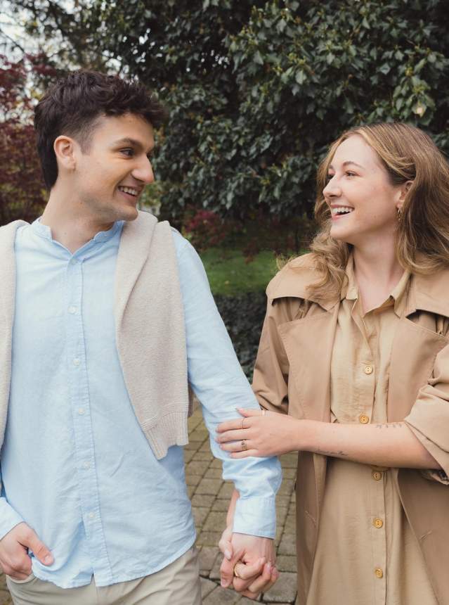 Young couple walking in arm along a brick pathway. Heritage home in the background.