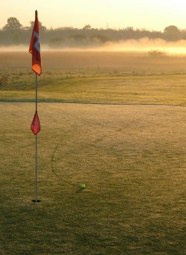 a golf course and hole in early morning mist