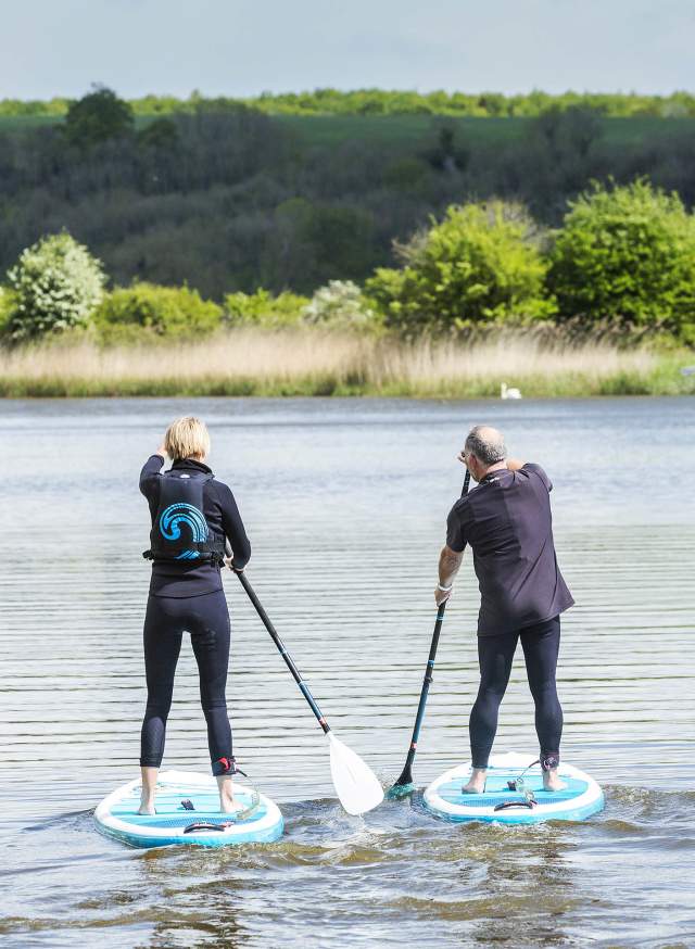 A couple stand up paddle boarding along a river in Sussex