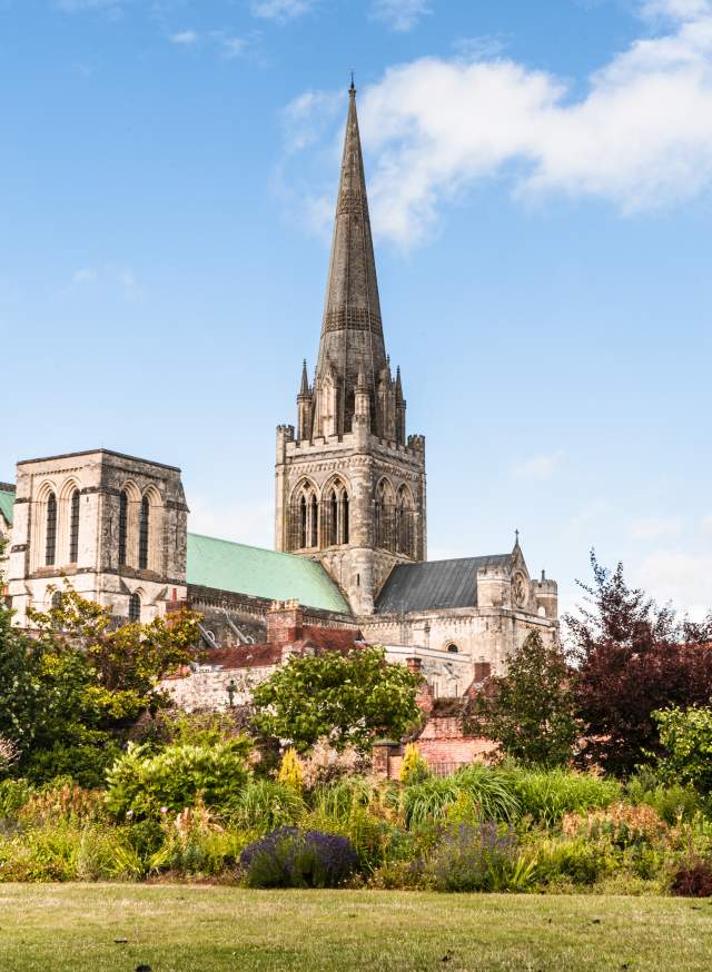 A view of Chichester Cathedral from the gardens with the spire reaching blue sky