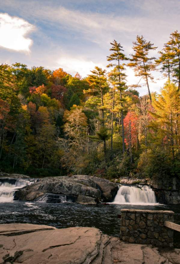 river cascades surrounded by colorful autumn forest beneath a partly cloudy sky.