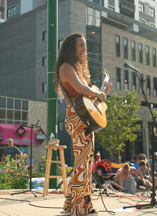 Women with guitar playing and singing on stage in the summer in downtown Lansing