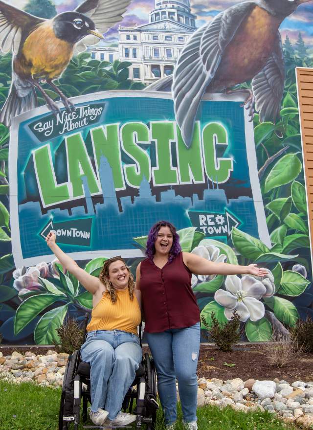 Two ladies in front of a "Say Something Nice Mural Lansing"