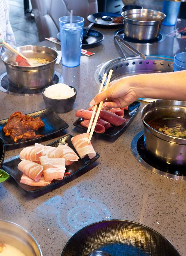 Plates of fresh vegetables, meats, and sauces ready for grilling at KPOT Korean BBQ & Hot Pot.”