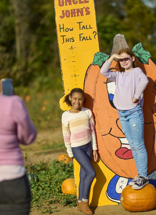 Two girls getting their picture taken in front of a cartoon pumpkin at Uncle John's Cider Mill