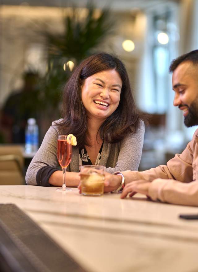 Relaxing together at the bar of Toscana Kitchen & Wine Market, a couple shares laughter and conversation in a cozy, welcoming atmosphere.