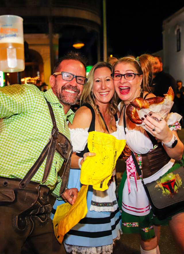 Two women and a man holding a beer bug and a pretzel