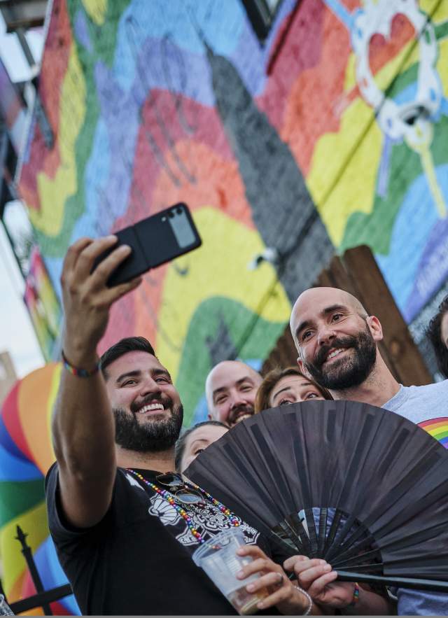 group of people taking a selfie in front of a rainbow mural