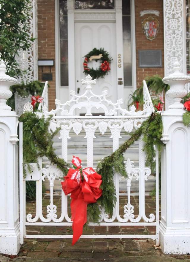 White cast iron fence with green leafy garland and red bows in front of a historic brick home