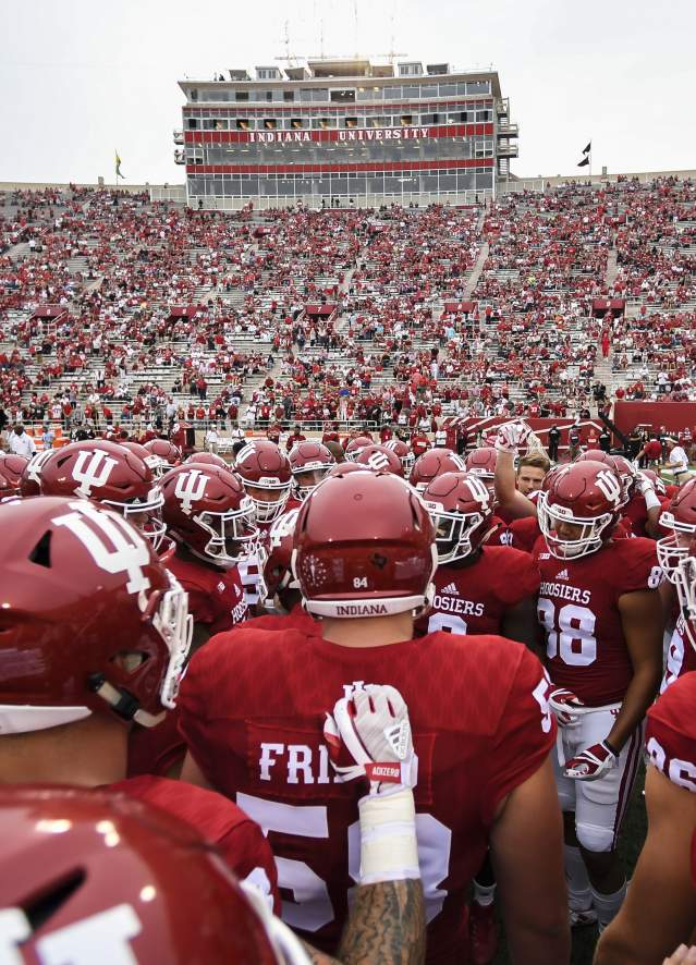 Indiana University football team huddled on the field before a game in a stadium filled with fans.
