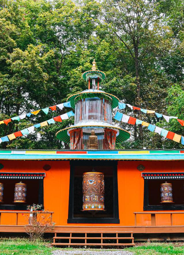 Colorful Mani Korlo prayer wheel at the Tibetan Mongolian Buddhist Cultural Center, surrounded by flags and greenery.