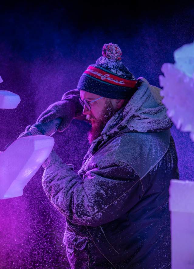 An ice sculptor using a power tool to carve a block of ice at the Freezefest ice battle