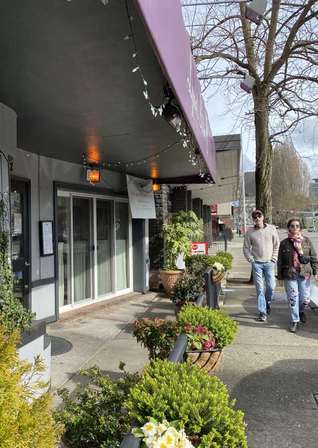 Two people walking on a sidewalk outside storefronts