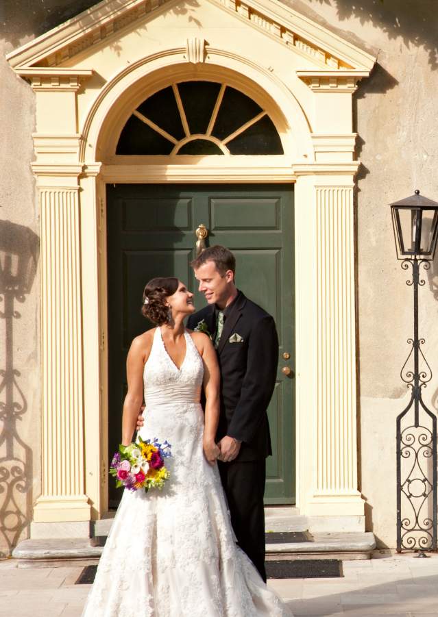 Woman in wedding dress holding bouquet next to man in a suit in front of the entrance to Hagley