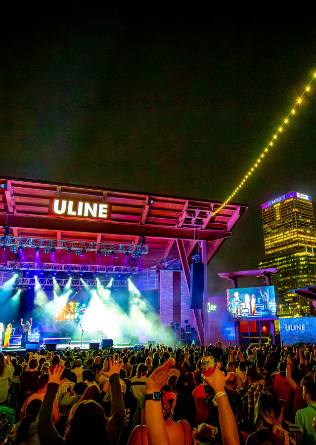 a photo of a concert stage with Milwaukee skyline behind it lit in rainbow colors for pridefest milwaukee