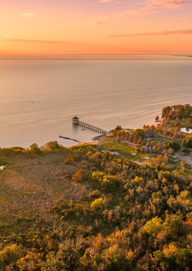 Aerial view of the Mandeville lakefront in Fontainebleau State Park and surrounding wetlands in fall, glowing beneath a warm sunset over Lake Pontchartrain.