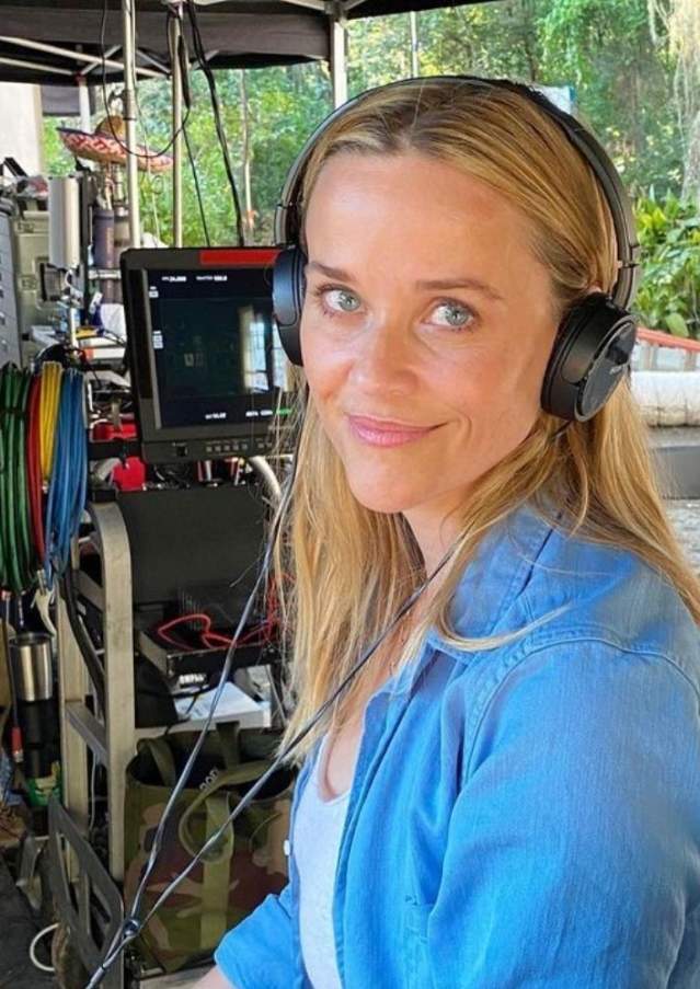 Reese Witherspoon on the film set of "Where the Crawdads Sing" wearing earphones with camera and sound equipment behind.