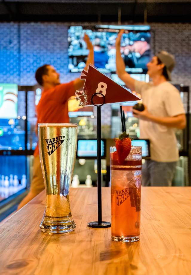 two guys high-fiving in a blowline alley with drinks in the foreground