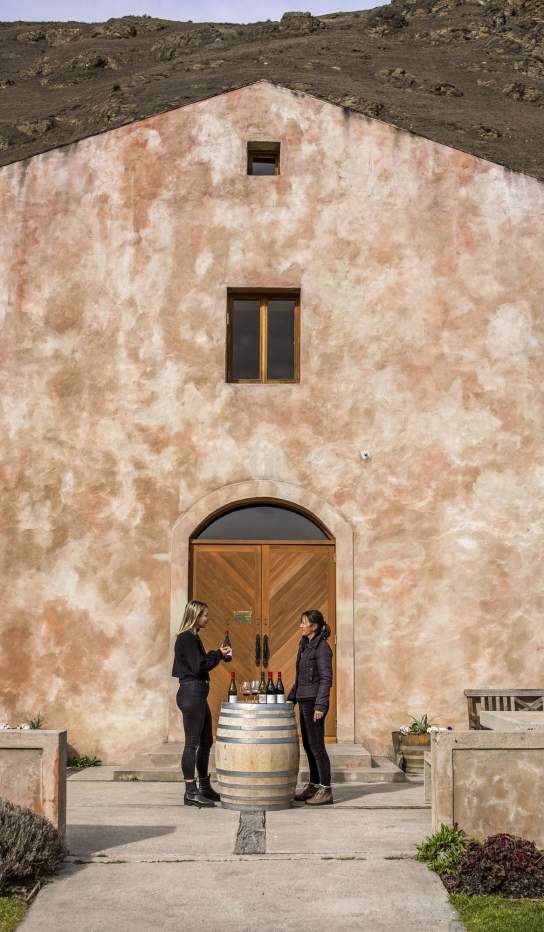 A person having a wine tasting outside Chard Farm Cellar door, a dusty pink Mediterranean style building