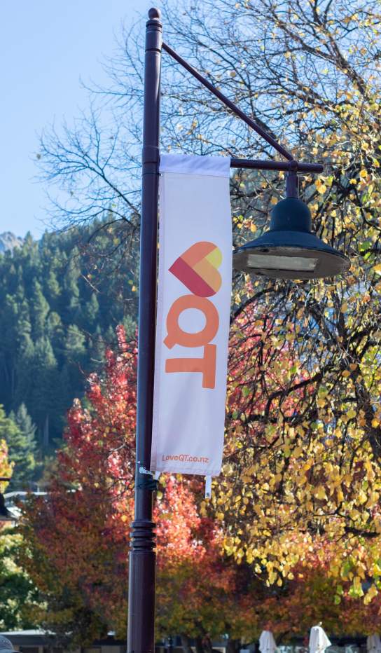 Love Queenstown flags displayed in the street with autumn trees and mountain in the background