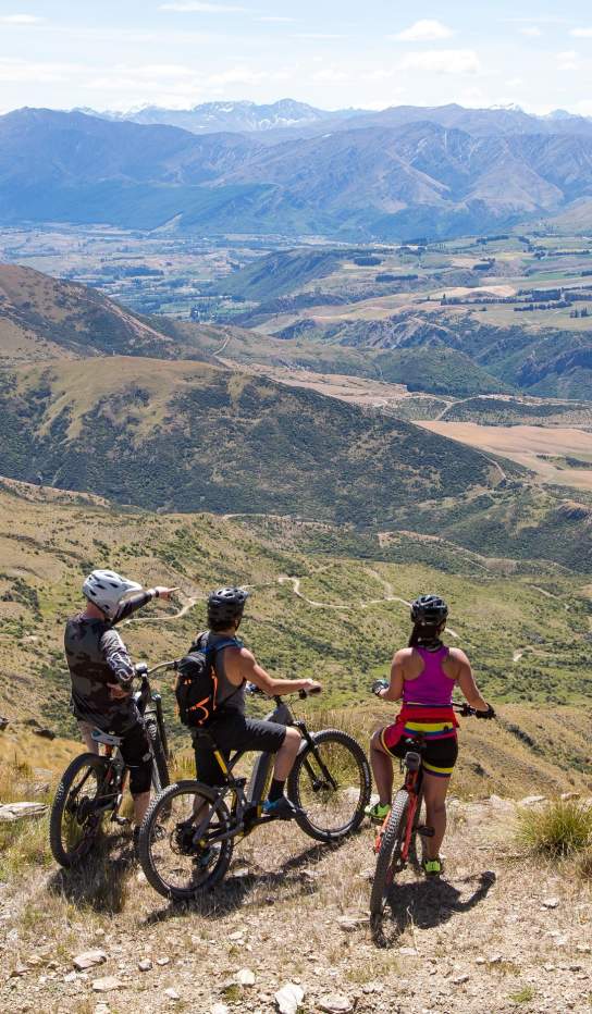 Three bikers standing on top of a mountain overlooking the mountain range and basin