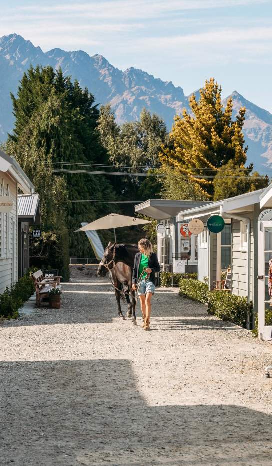 A lady walking a horse on a path lined with boutique cabins and shops
