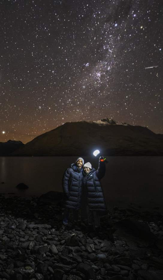 Two people holding a light with a background of mountains and a starry night sky