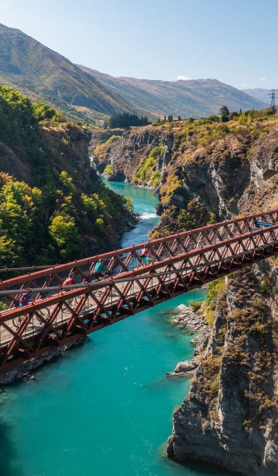 People biking over a bridge with vibrant blue water below