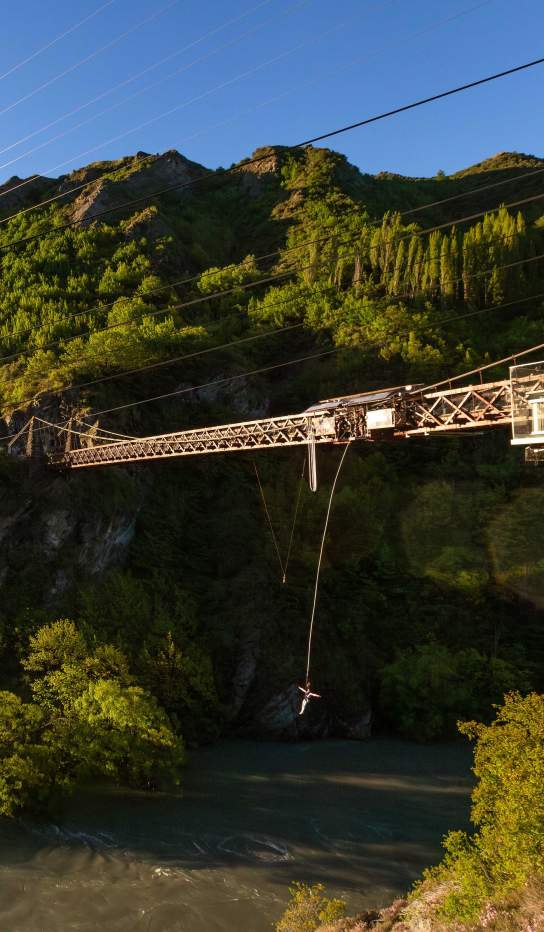 Wide shot of someone bungy jumping off a bridge over a river
