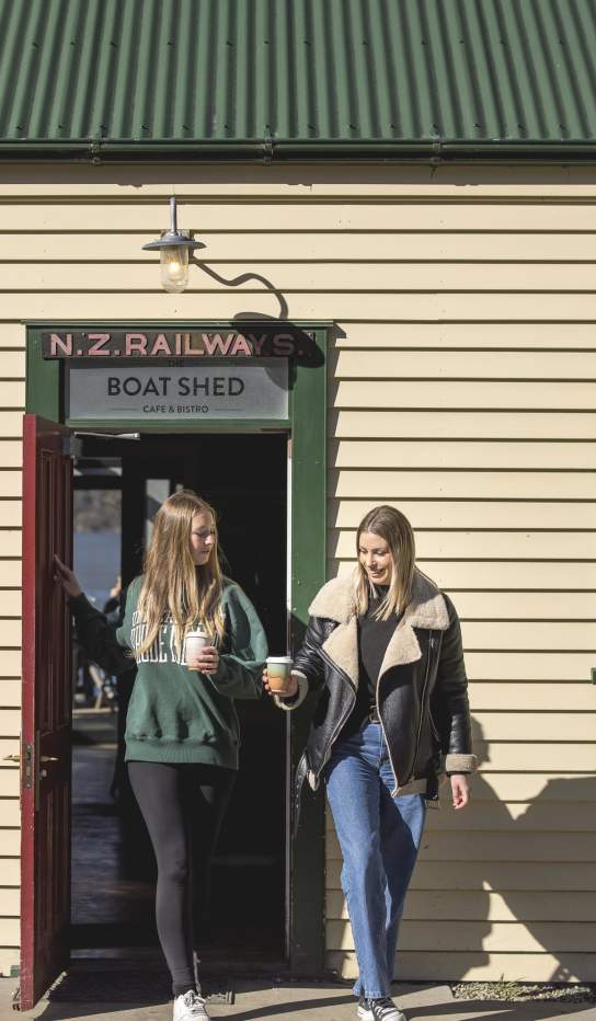Two people walking out of the Boat Shed Café with keep cups
