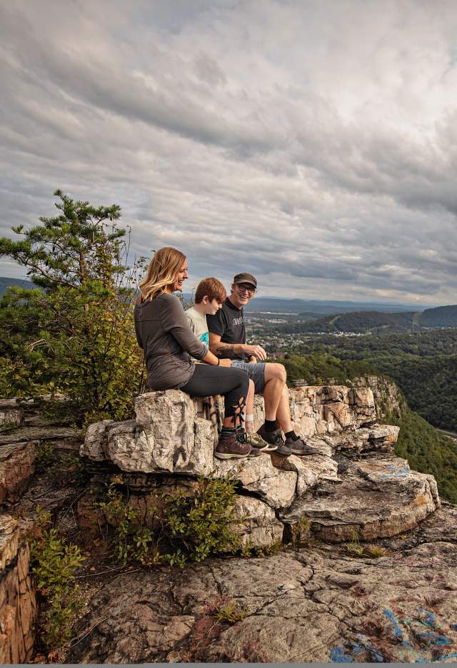 A mom, dad and son sit on a shale cliff overlooking a mountain vista.