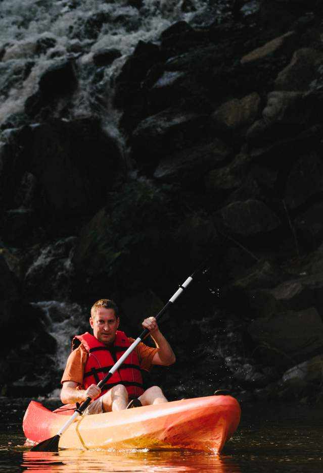 a man wearing a life-jacket and kayaking with a waterfall in the background