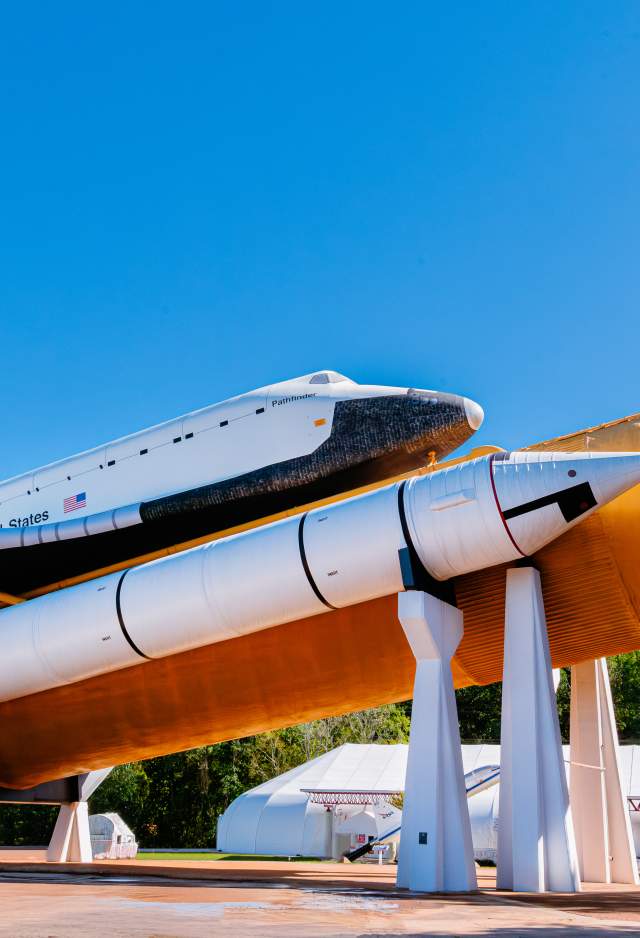 The Space Shuttle Pathfinder is displayed atop a full-scale external tank and solid rocket boosters at the U.S. Space & Rocket Center in Huntsville. The shuttle and rocket stack stand against a clear blue sky, showcasing the scale and engineering of NASA’s Space Shuttle program.