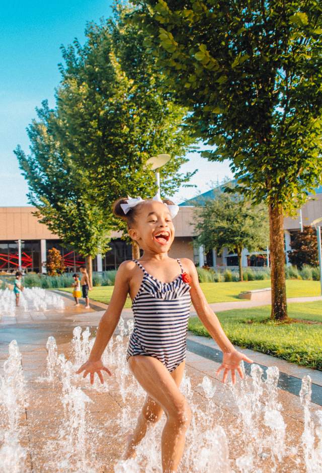 Girl playing outside in water fountain