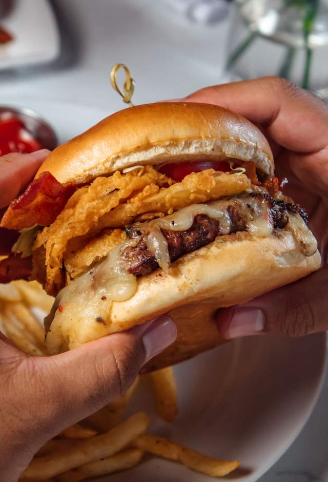 hands holding burger from Rouj Creole