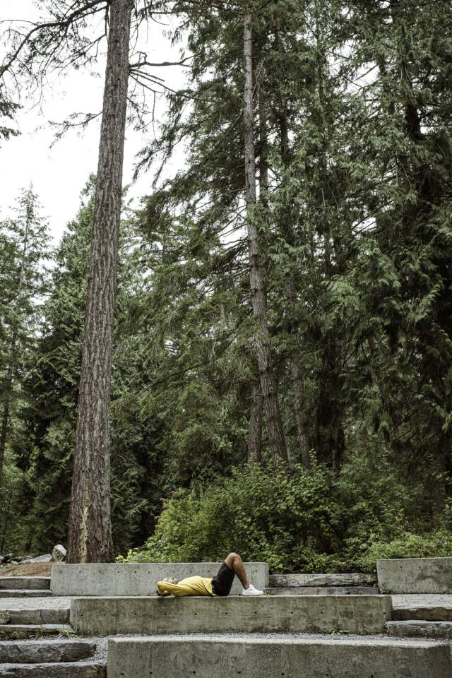 Person lying on a concrete bench in a forested park.