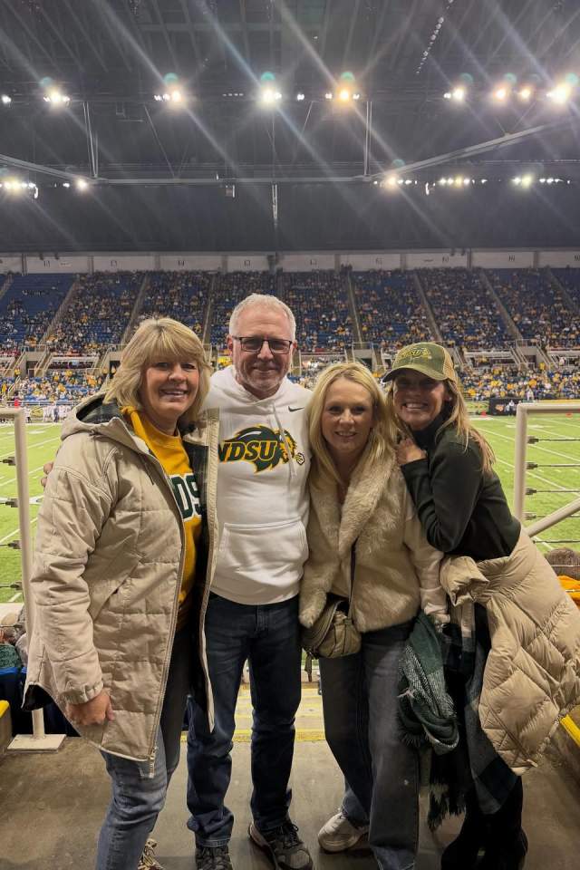 Four people standing in front of NDSU football field at the FARGDOME.